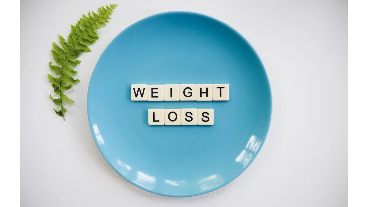 Blue plate with letter tiles spelling weight loss beside a green leaf