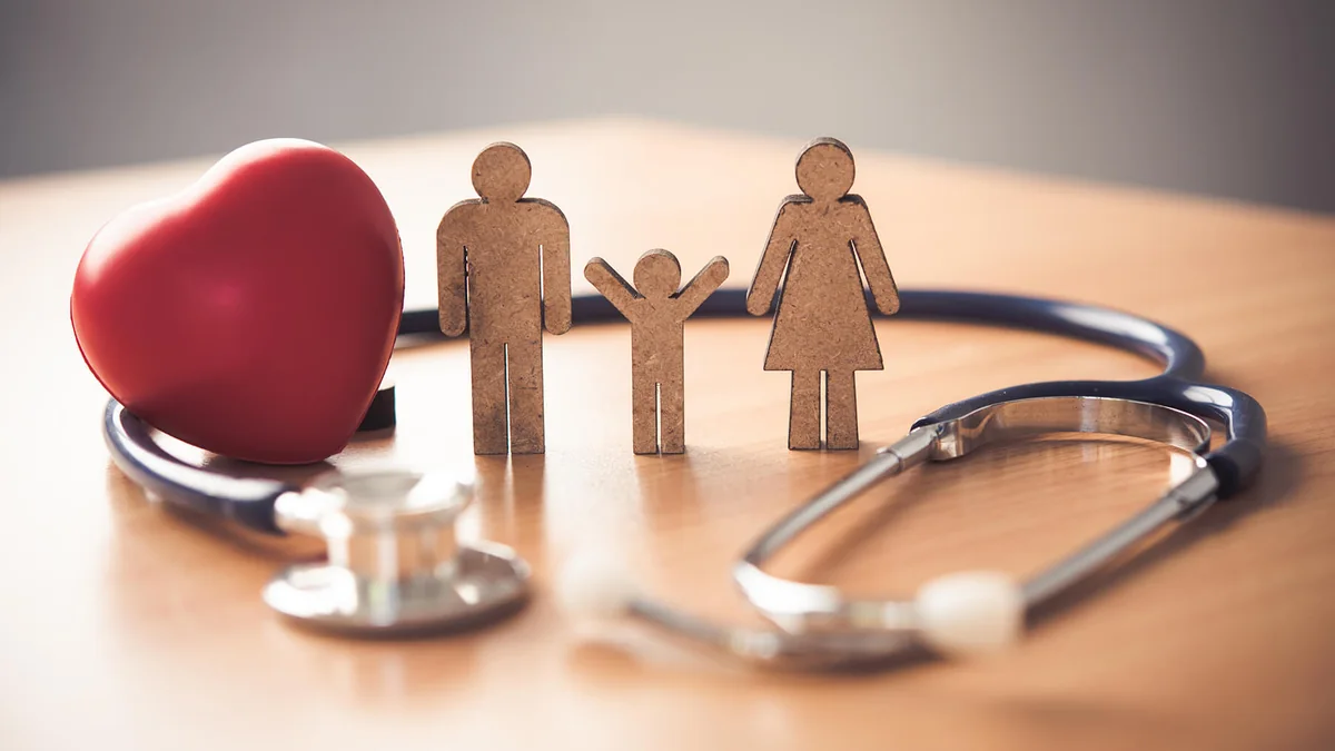 Stethoscope, red heart and wooden family figures on a table